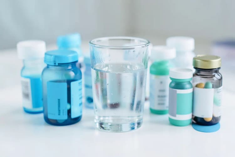Uma caixa de medicamentos variados e um copo d'água.