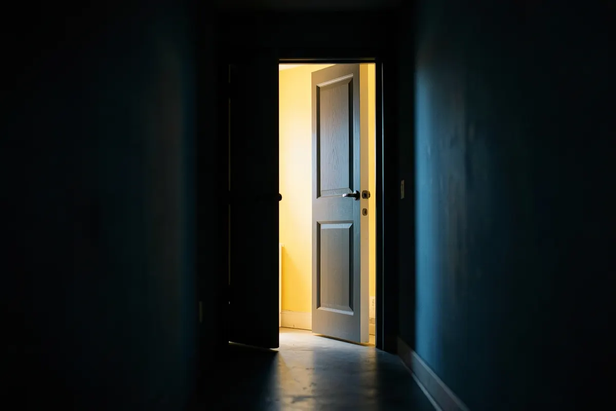 Uma porta entreaberta com uma luz suave emanando do interior, em um corredor escuro.